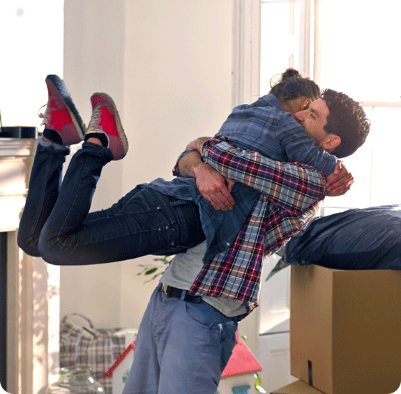 A man smiling lifting up a woman whilst moving into a new house