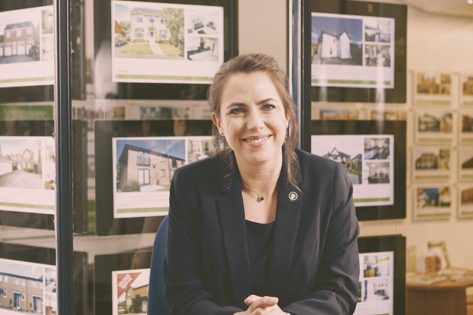 Lady with an estate agency window showing properties in the background