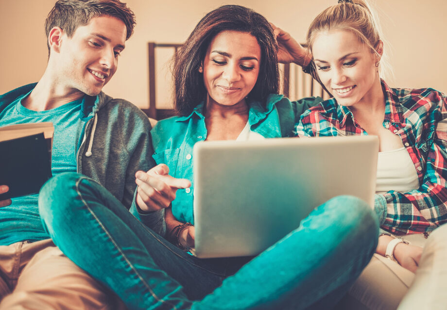 Three people looking at a laptop whilst sat on the sofa