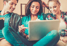 Three people looking at a laptop whilst sat on the sofa