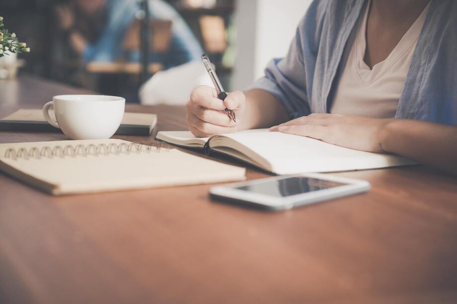 Person writing in a notebook sat at a table