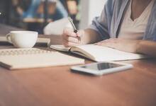 Person writing in a notebook sat at a table