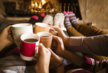 People sat in front of a fireplace with mugs of tea/coffee
