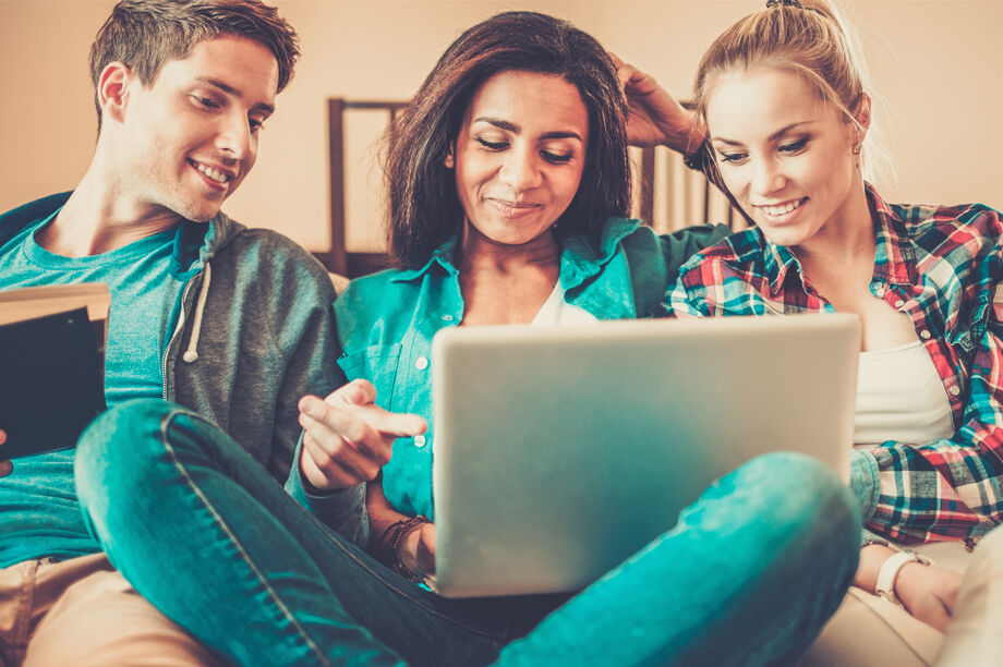 A group of teenagers siting on the sofa looking at a laptop