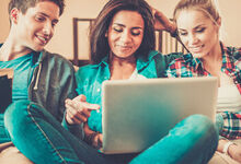 A group of teenagers siting on the sofa looking at a laptop