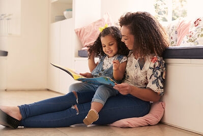 A mother and daughter reading a children's book on the floor