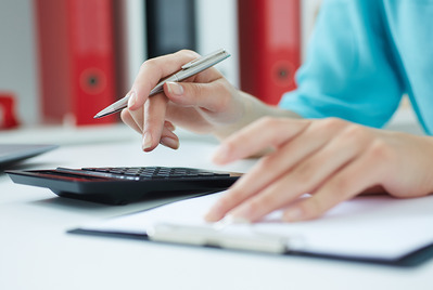 A pair of hands, one holding a pen and using a calculator