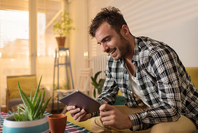 Man on sofa, smiling at tablet