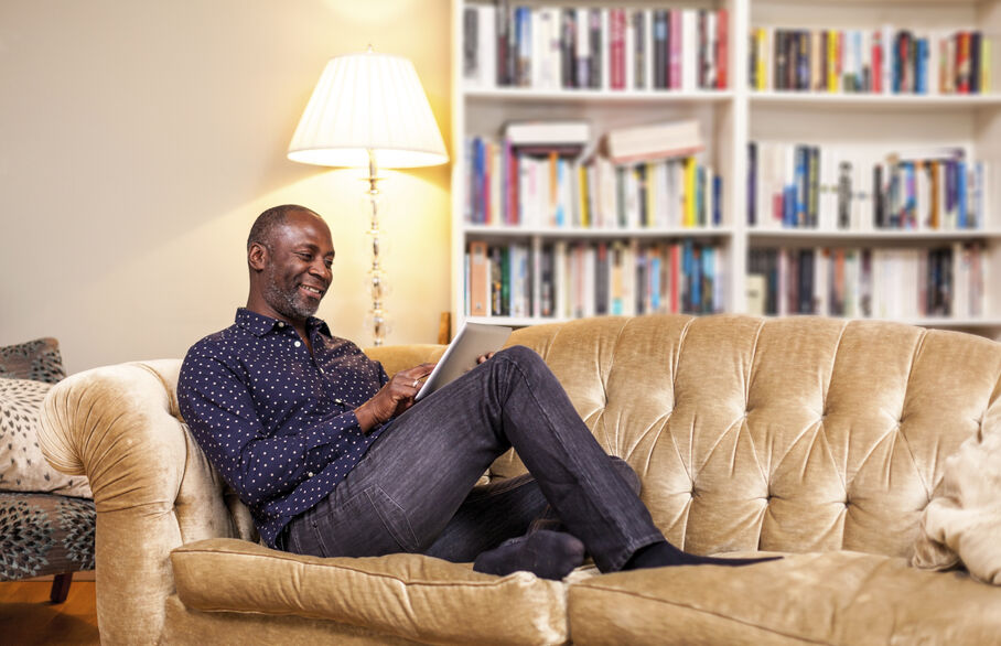 Person sat on a sofa with their feet up looking at a tablet computer