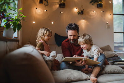 Man reading to two young children on teh sofa at home
