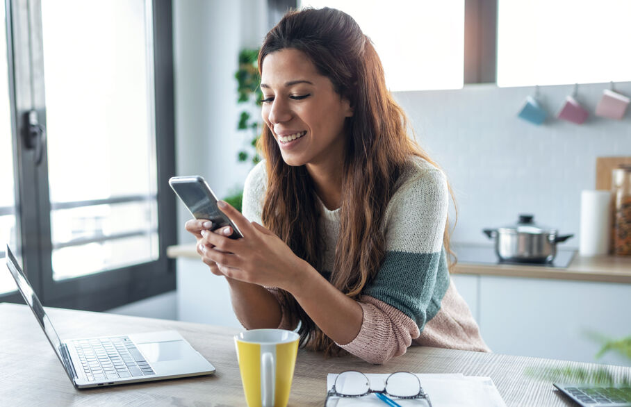 Person sat at a table with laptop and looking at phone