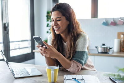 Person sat at a table with laptop and looking at phone