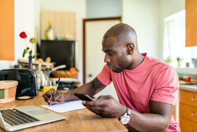 Person looking at a phone and laptop sat at a table