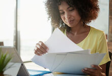 Lady shuffling paper work whilst sat in front of a computer