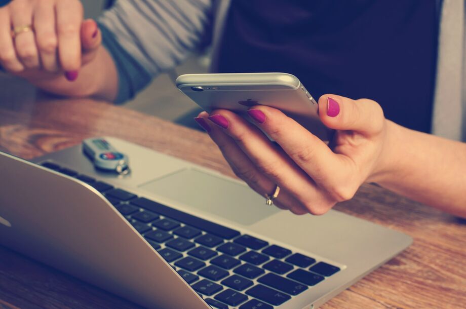 Person at their laptop whilst also reading from their mobile phone