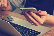 Person at their laptop whilst also reading from their mobile phone