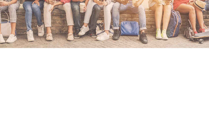 Students sitting in a row with phones, drinks and backpacks