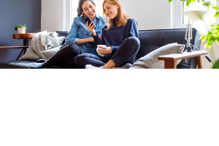 Two women relaxing together on a sofa while looking at a phone